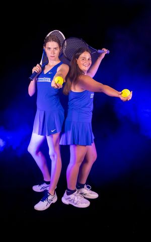 Two tennis players in matching blue outfits pose back-to-back with tennis balls.