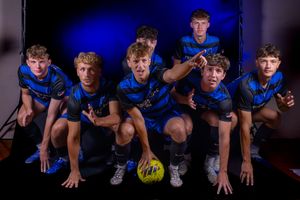 Soccer players in light blue uniforms crouch in dynamic formation under dramatic studio lighting.