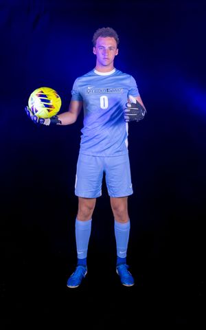 Soccer players in light blue jerseys hold yellow balls while posing against dark backdrop with blue lighting.