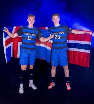 Soccer team members hold flags while posing in blue uniforms against dark background.