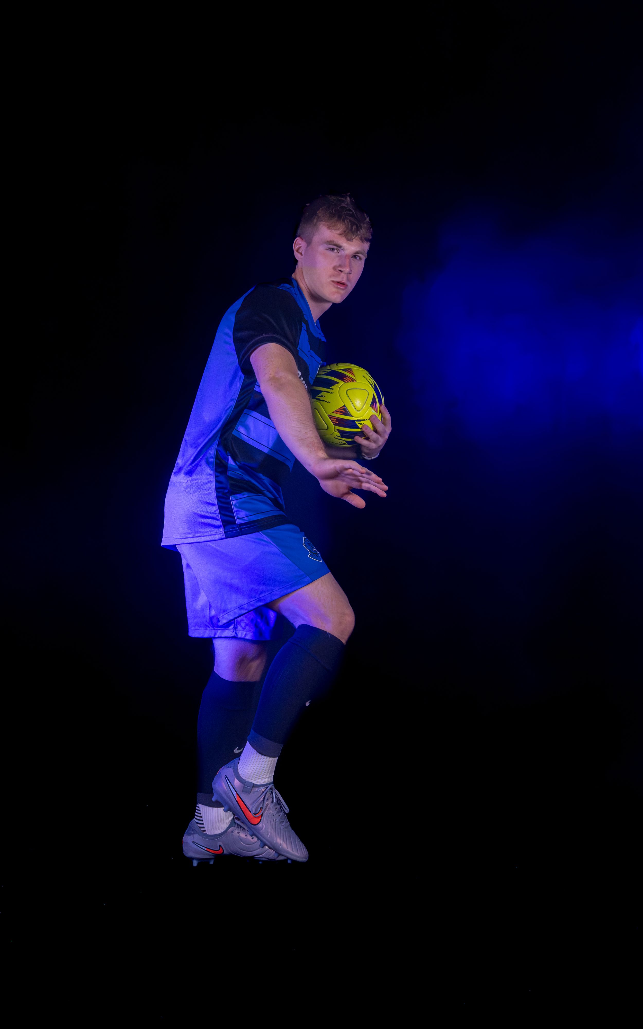 Soccer player performs dynamic ball handling moves under dramatic blue lighting with fog effects.