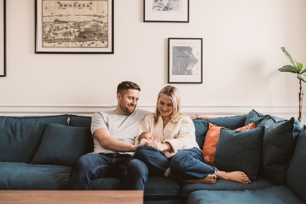 A couple sitting together on a navy blue sofa while looking at their newborn baby.