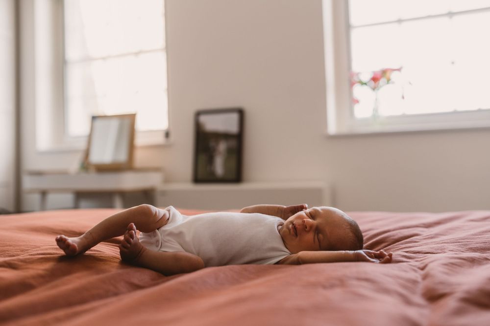 A newborn baby sleeps peacefully on rust coloured bedding.