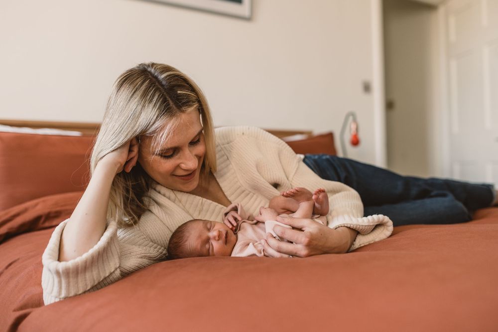 Mother and newborn baby share tender moment while relaxing together on a bed.