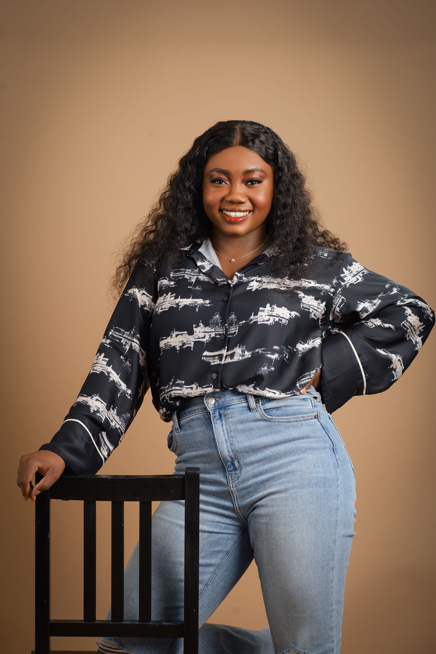Casual fashion photoshoot featuring black patterned sweater and light wash jeans against tan backdrop.