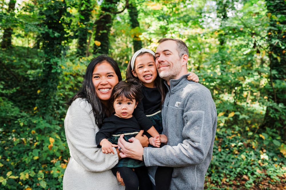 A happy family embraces and smiles together in a lush green forest setting during an outdoor photo session.