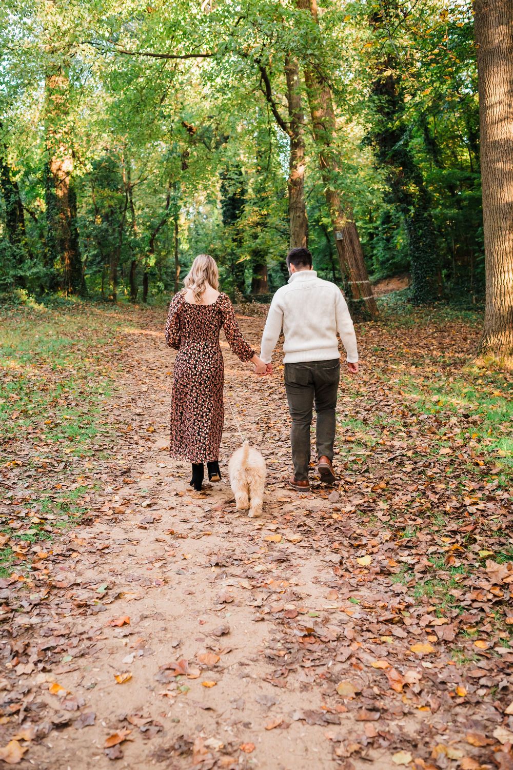 A couple and child walk along a leaf-covered forest trail during autumn creating a scenic outdoor family moment.