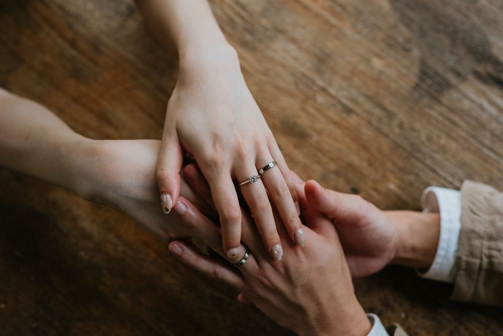 Close-up detail shot of hands with rings on weathered wooden surface.