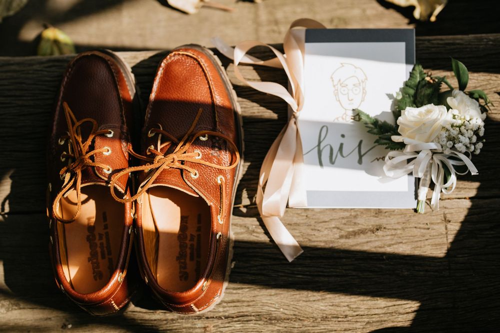 Brown leather wedding shoes displayed with decorative name cards and floral elements.