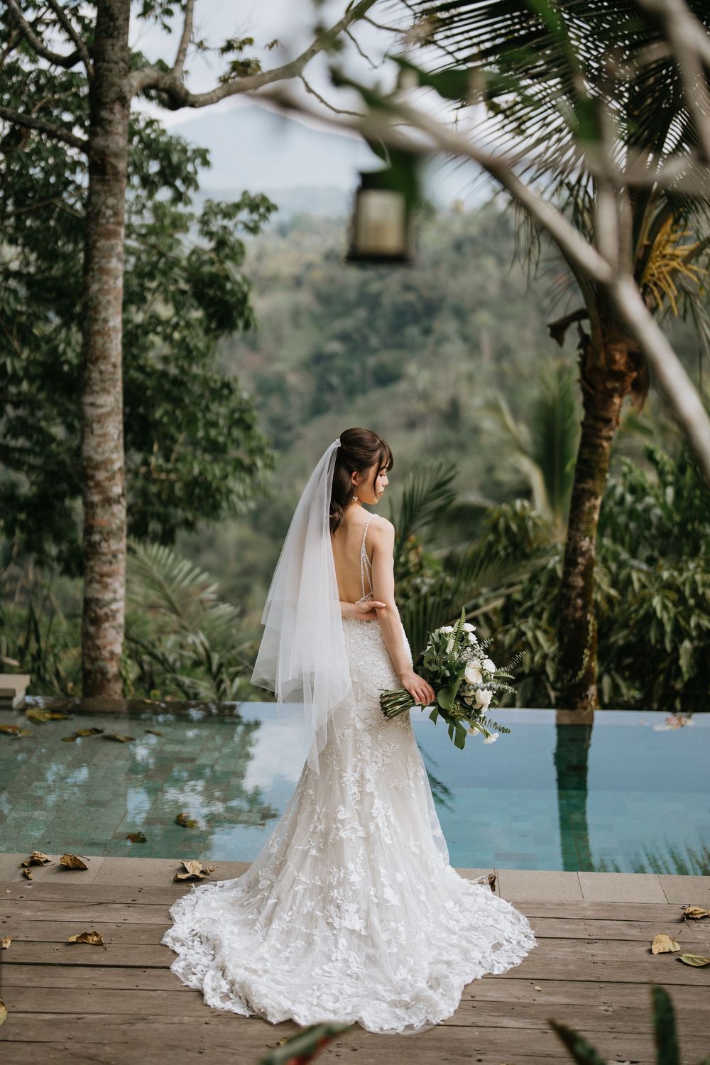 A stunning white lace wedding dress photographed against a tropical backdrop with palm trees.