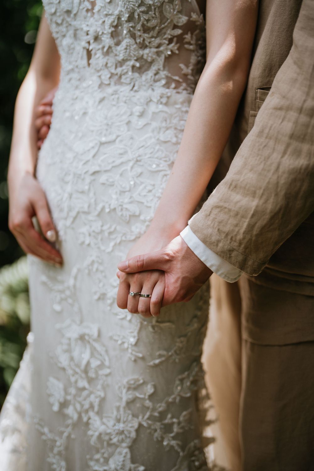 Close-up detail of white lace wedding dress next to tan linen suit.