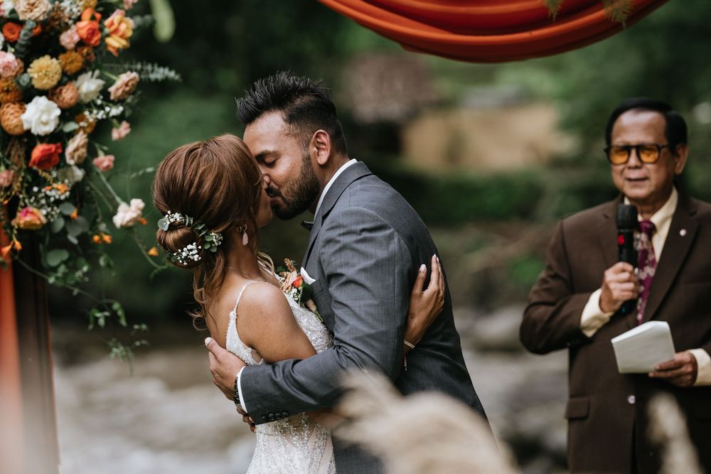 Outdoor wedding ceremony with coral and peach floral arrangements under natural greenery.