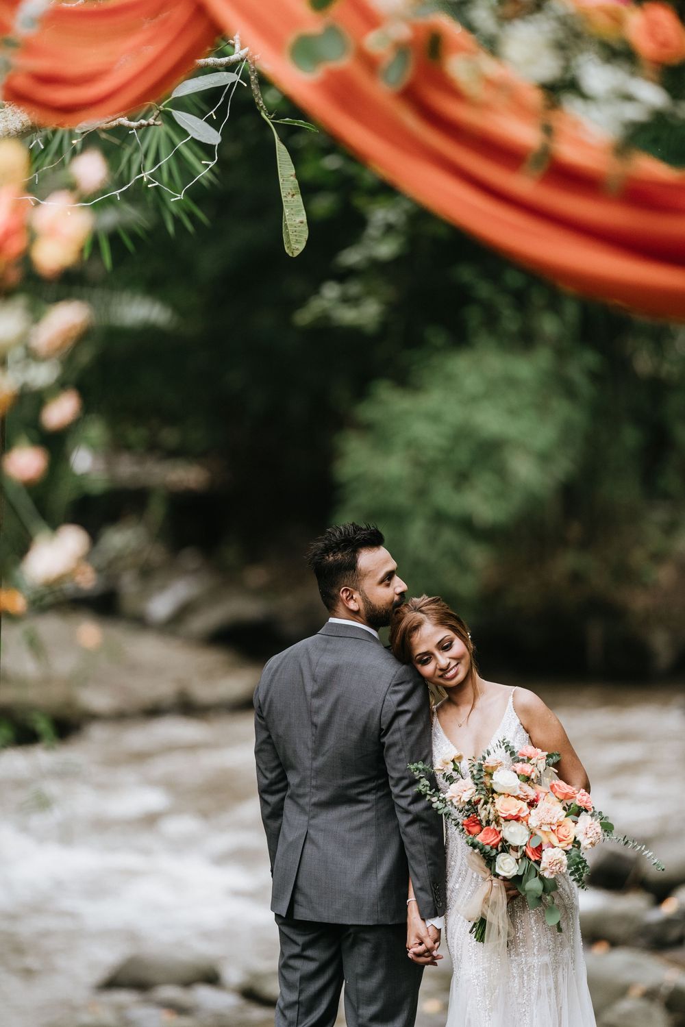Romantic wedding portraits under coral draping with peach and white floral bouquet.
