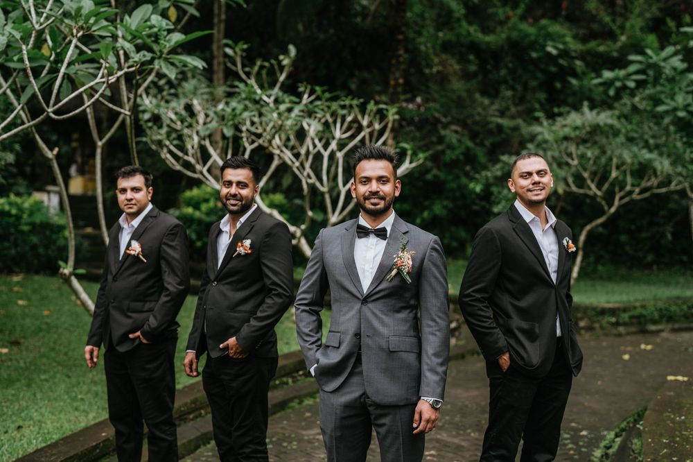 Groomsmen in dark suits posing together at outdoor garden wedding.
