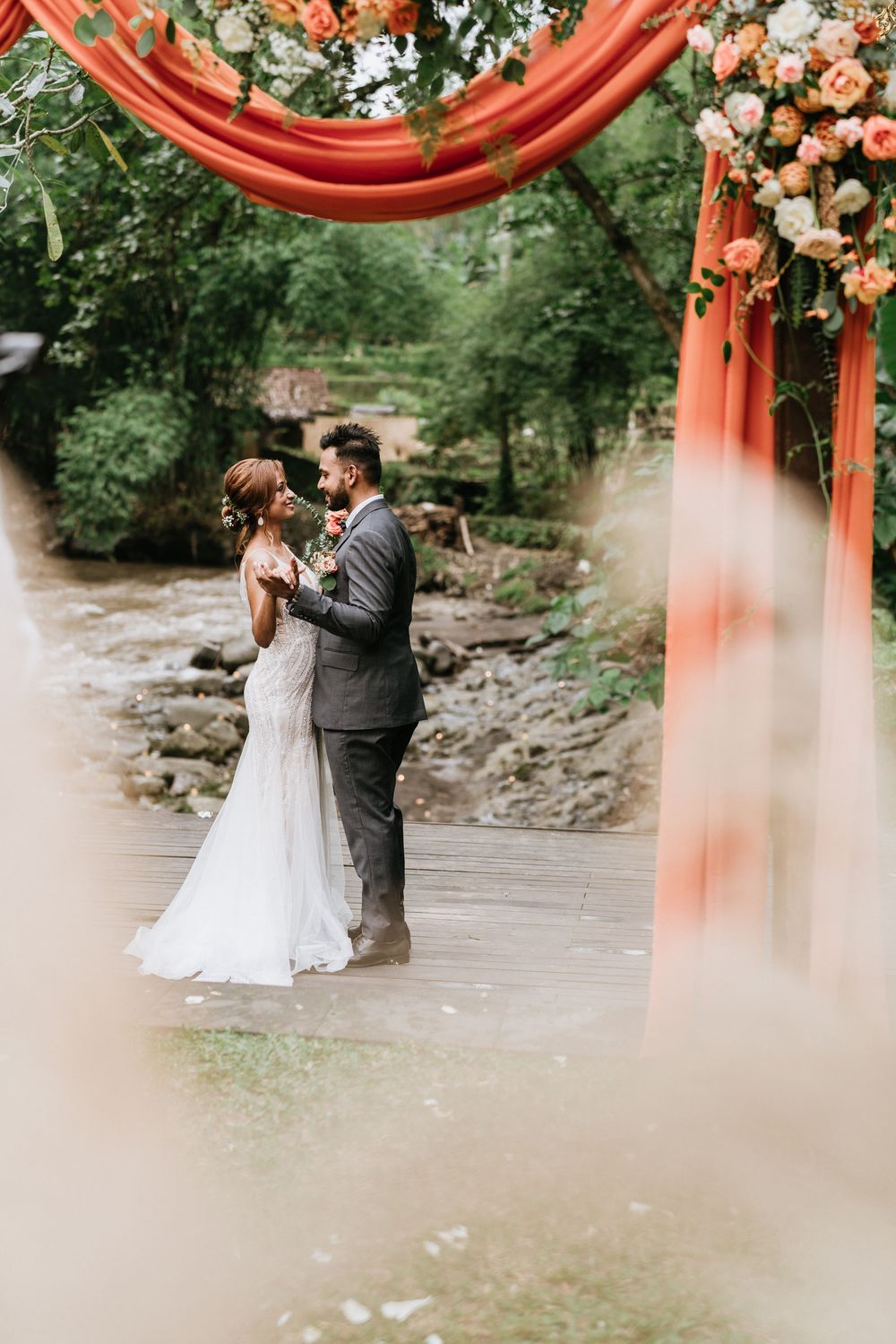 Romantic wedding ceremony moment beneath an orange floral arch with lush greenery in the background.