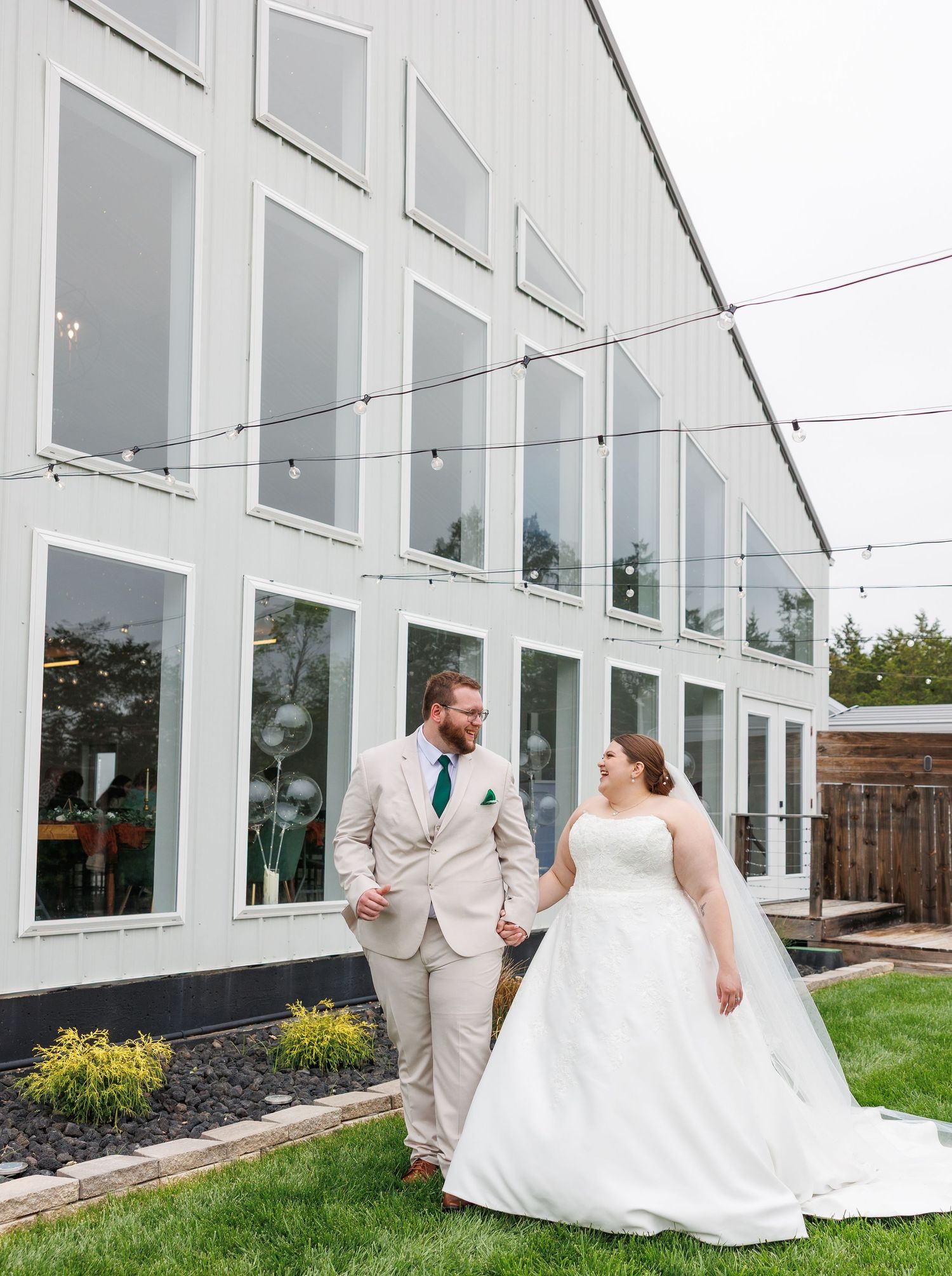 A wedding couple shares a joyful moment outside a modern white building with large windows and landscaped grounds in Branson, Missouri.