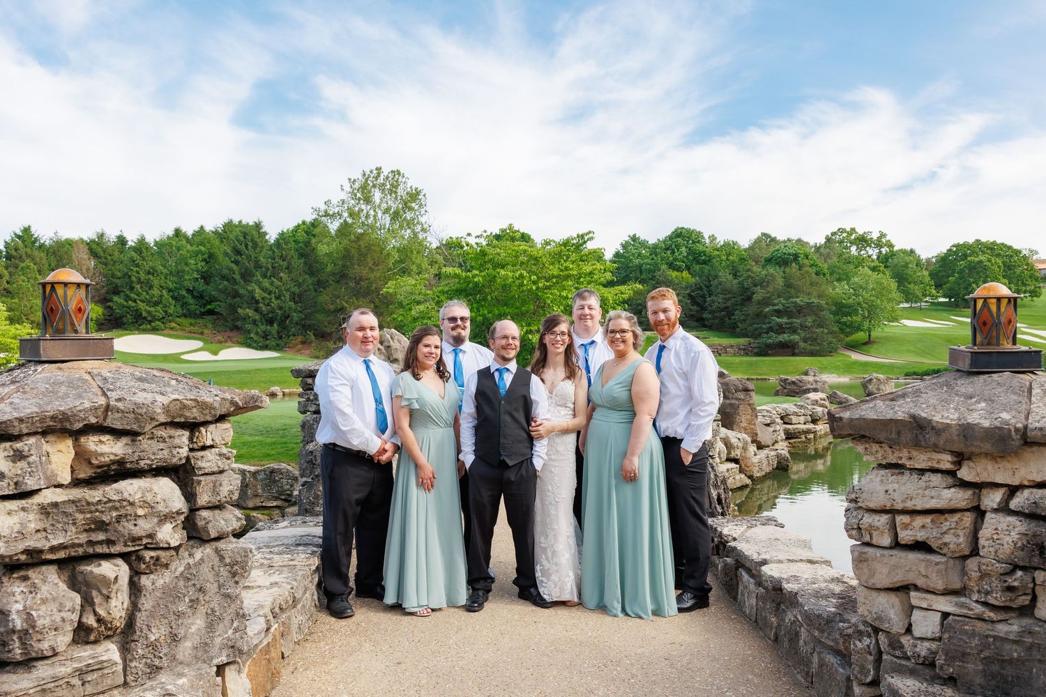 Wedding party poses in front of rustic stone wall for outdoor photos on a beautiful summer day by Janie Loftin Photography.