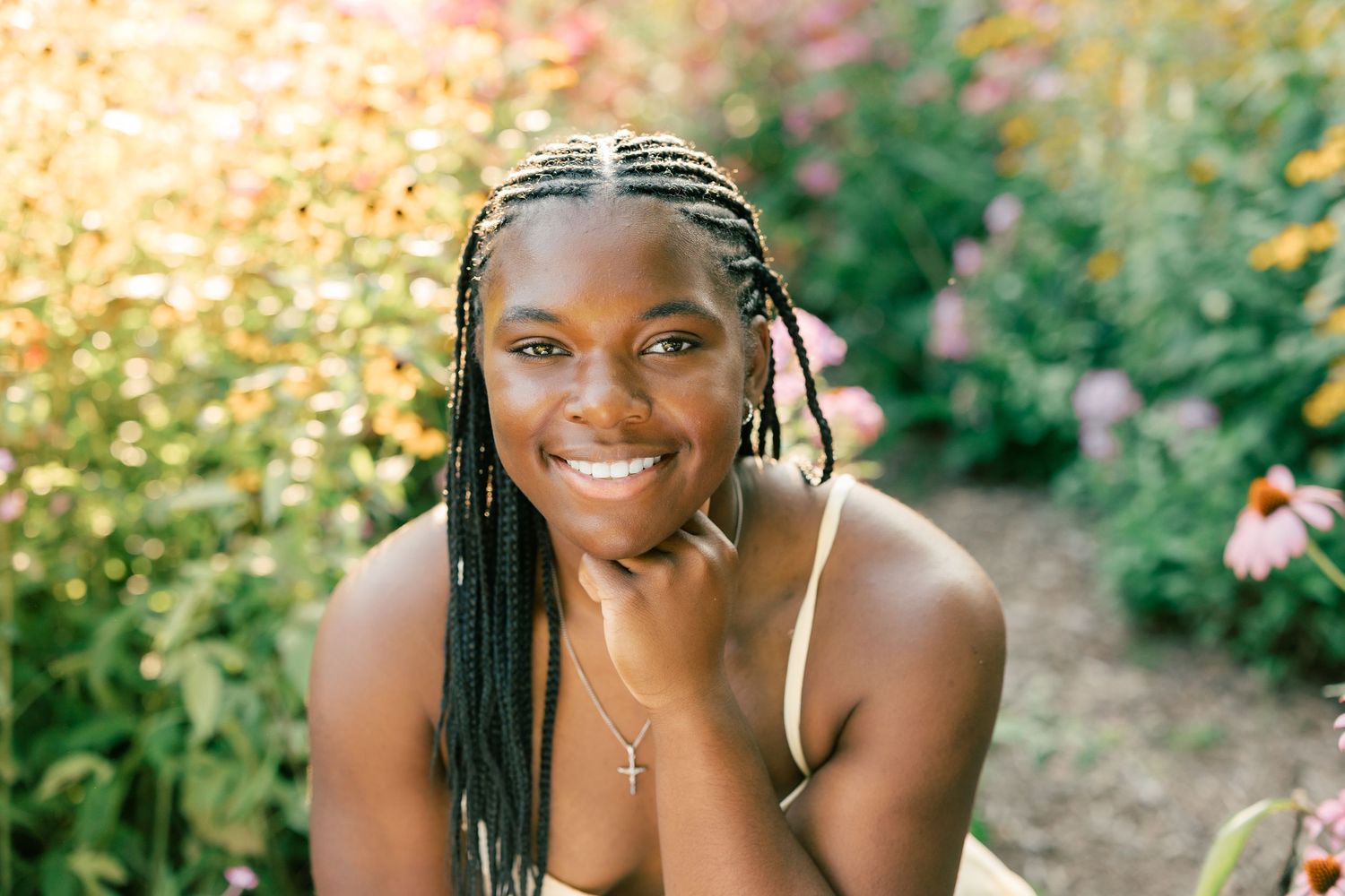 Person with braided hair smiling brightly in a garden setting during golden hour.
