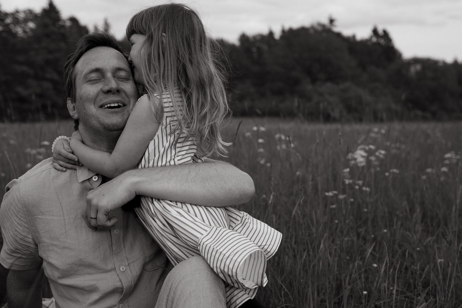 little girl hugging her father who is smiling during outdoor family photo shoot in Stockholm