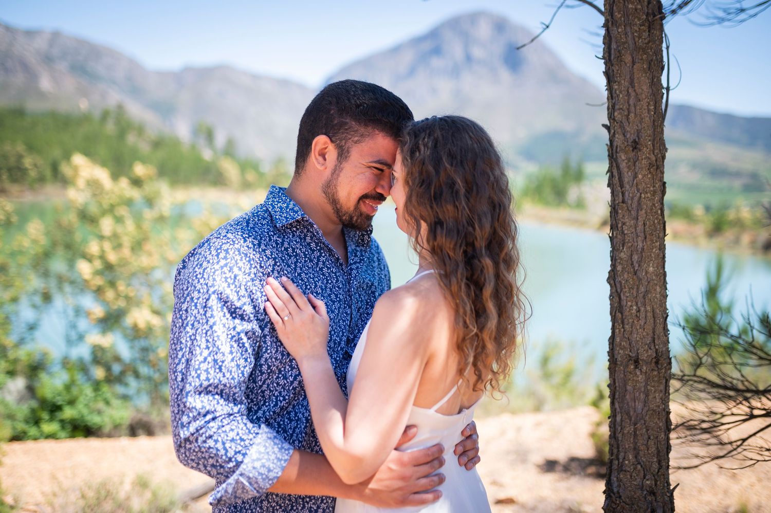 A romantic engagement photoshoot at sunset with a mountain lake backdrop amidst pine trees.