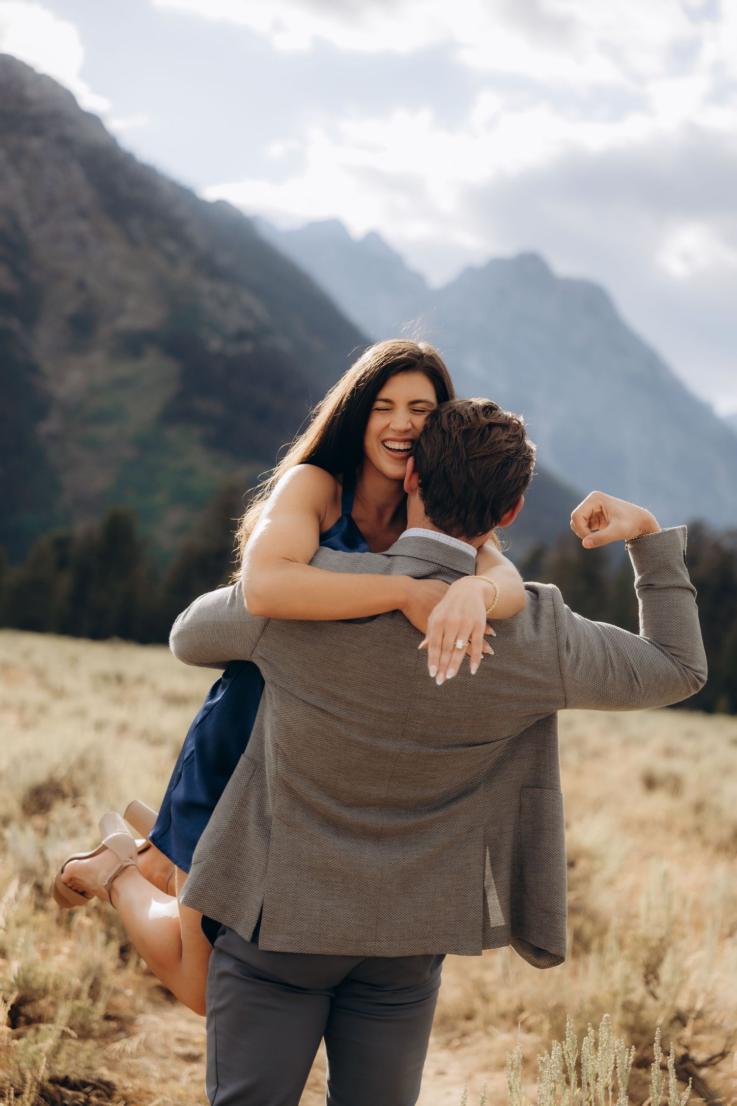 A couple shares playful and intimate moments against a backdrop of majestic mountains in a golden field at sunset.
