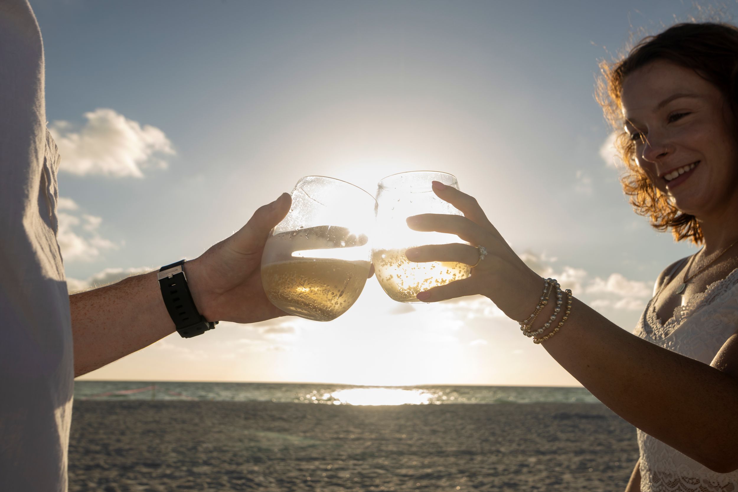 Couple toasting with champagne glasses at sunset on a tropical beach, celebrating a romantic occasion.