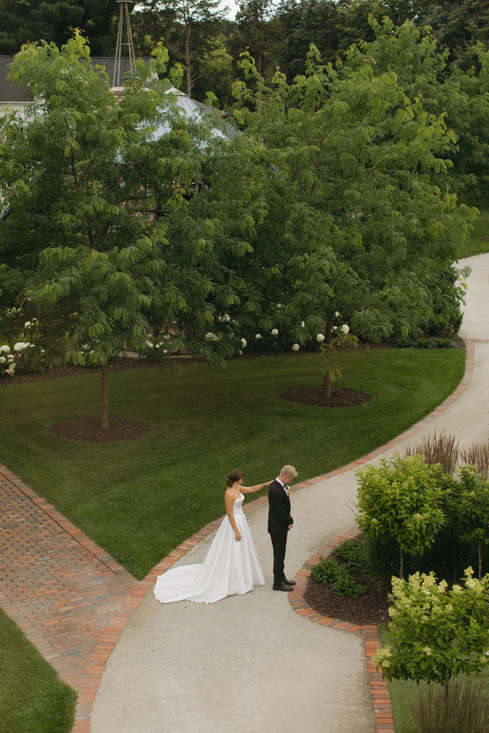 Wedding couple walking along a curved brick path surrounded by lush garden landscaping.