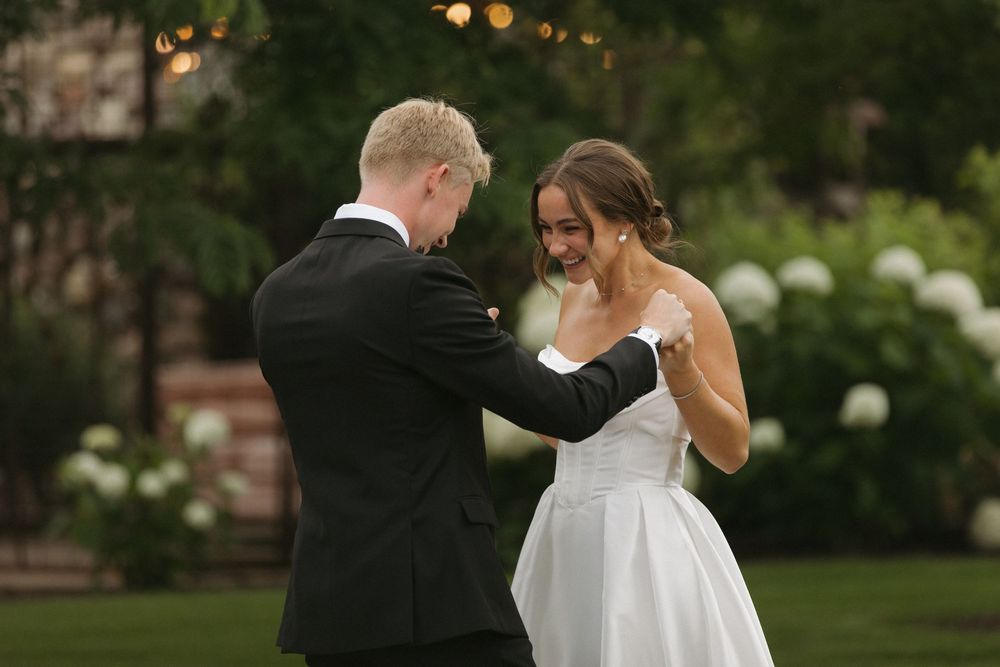 Wedding couple walking together on a garden path at dusk with warm lighting.