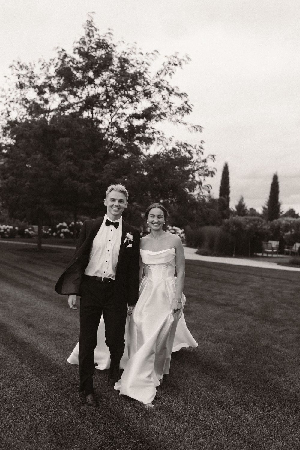 Black and white photo series of couple walking playfully across a grassy field.