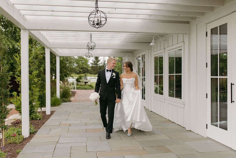 Newlyweds walk through a bright white covered walkway with elegant architectural details.