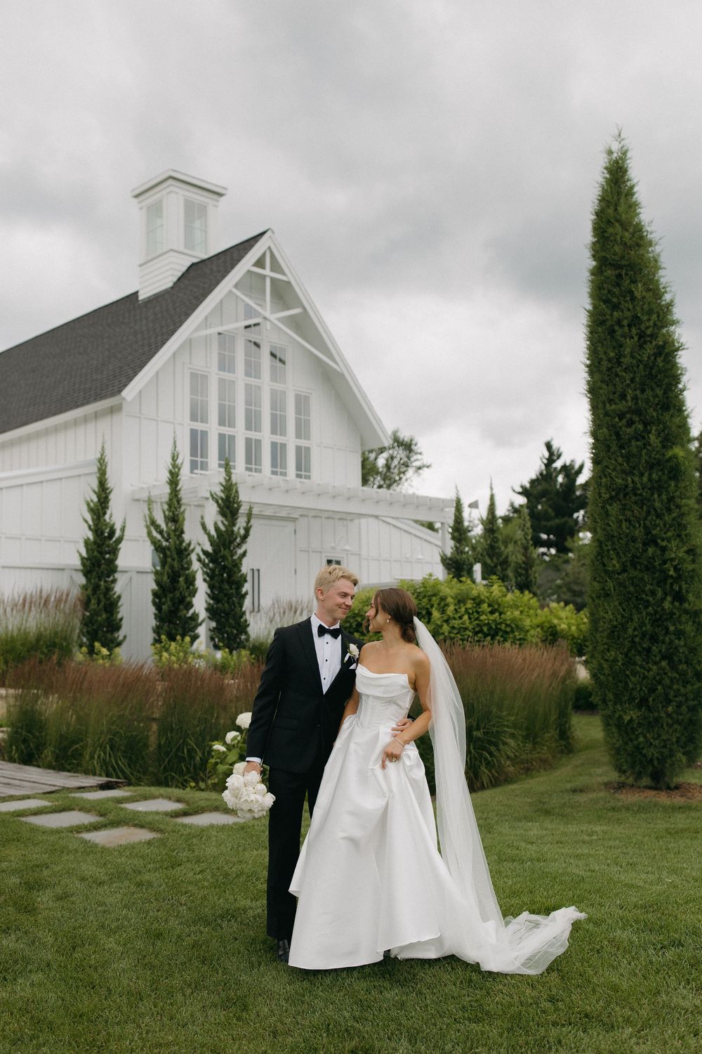 Wedding portraits captured in a garden setting with a white chapel building in the background.