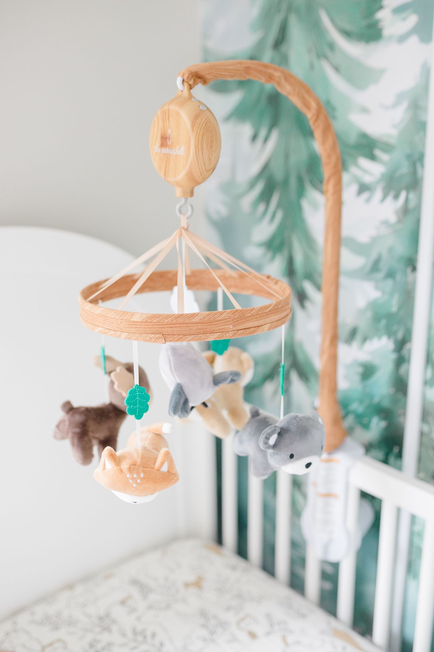 A wooden baby mobile with plush animal toys hangs above a white crib in a nursery.