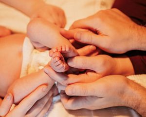 Family gathered around new born baby. Details of hands and babies feet.
