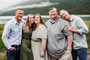 5 older siblings grouped together for a family photos. 3 bothers and 2 sisters all dressed in green and blue tones, standing by the water.