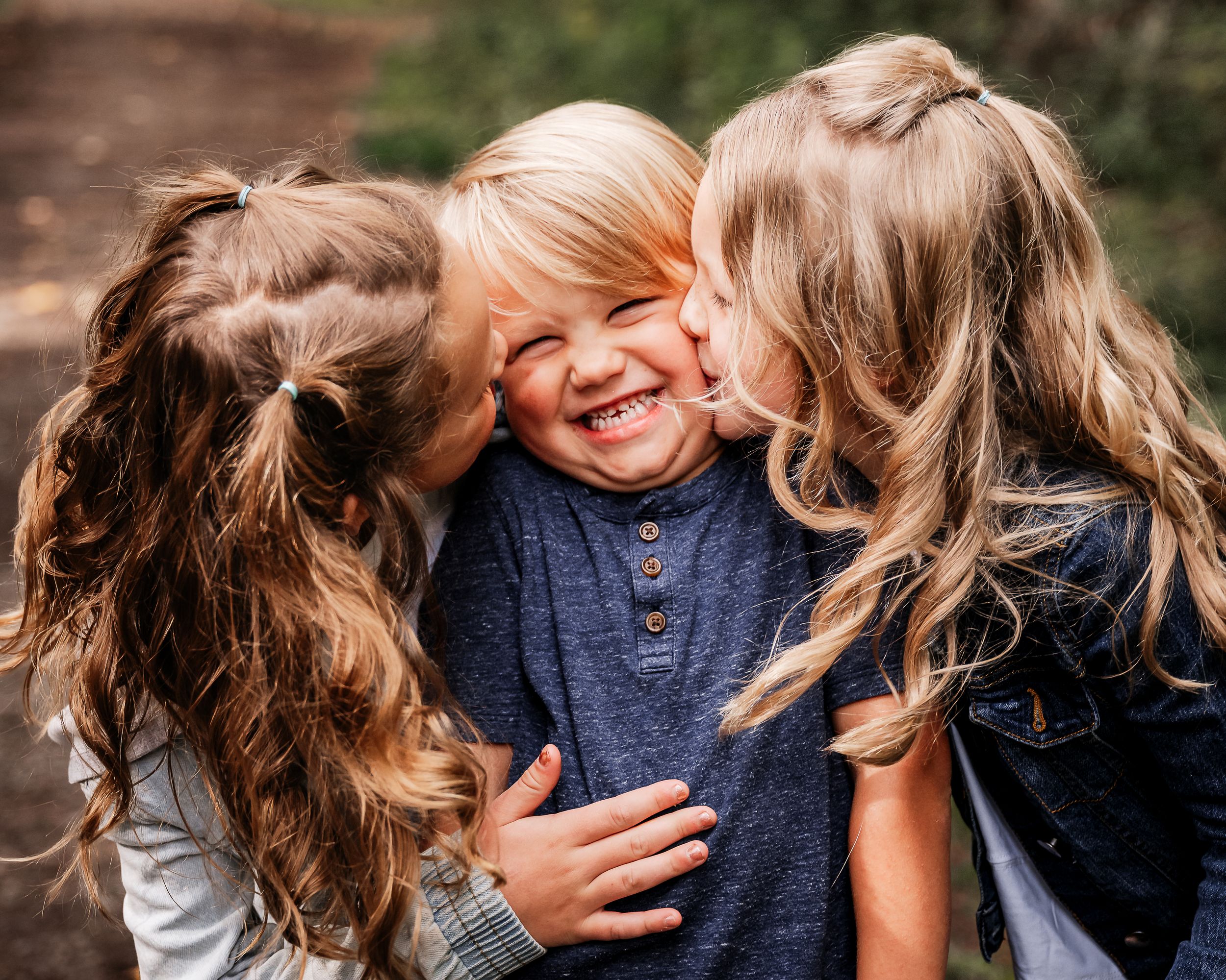 Big sisters giving little brother kisses on the cheeks.