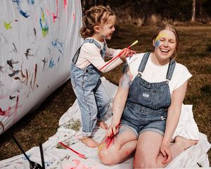 Playful lifestyle family photo—child painting on mom outdoors, capturing joy, laughter, and authentic connection.