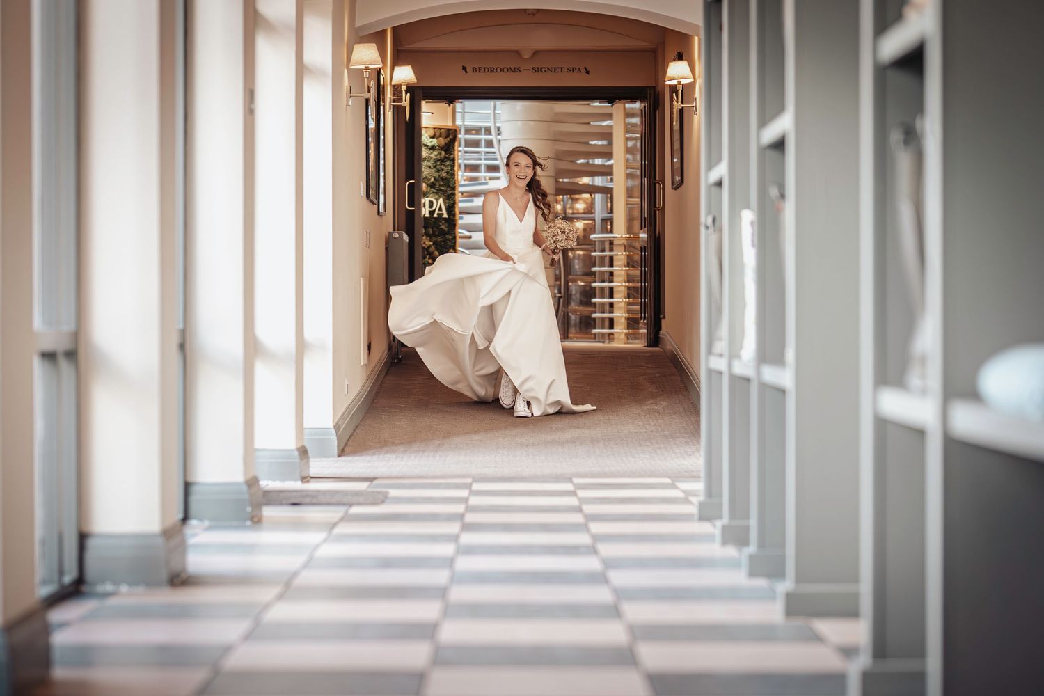 White wedding dress flowing in an elegant hallway with checkered floor.