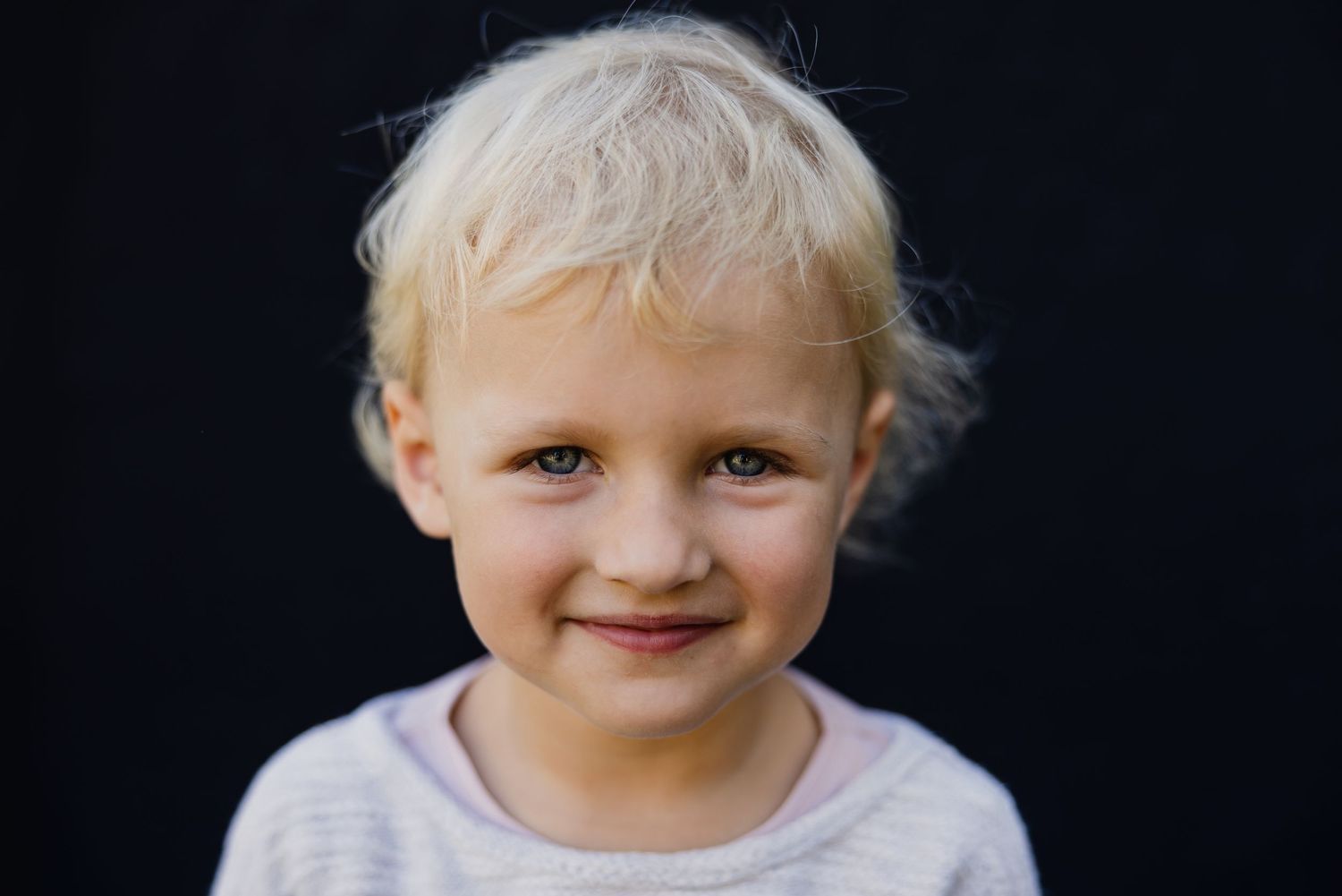 Sweet baby with light blonde hair and pink cheeks photographed in a series of candid expressive shots against dark background.