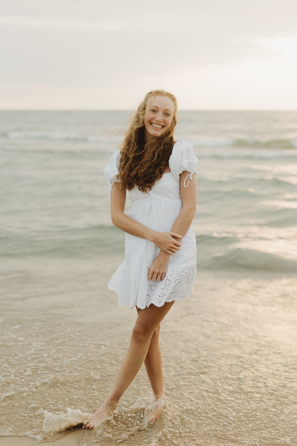 Child in white lace dress plays and splashes joyfully at the beach during golden hour.