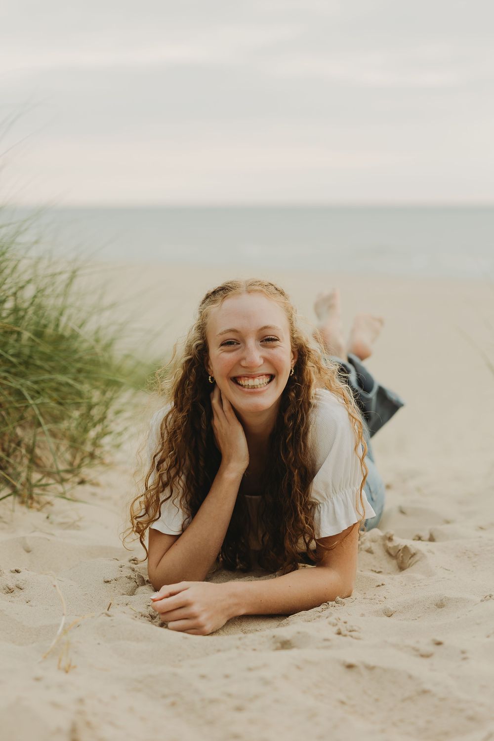 A person with curly hair lies on a sandy beach smiling, photographed from multiple angles in sequence.