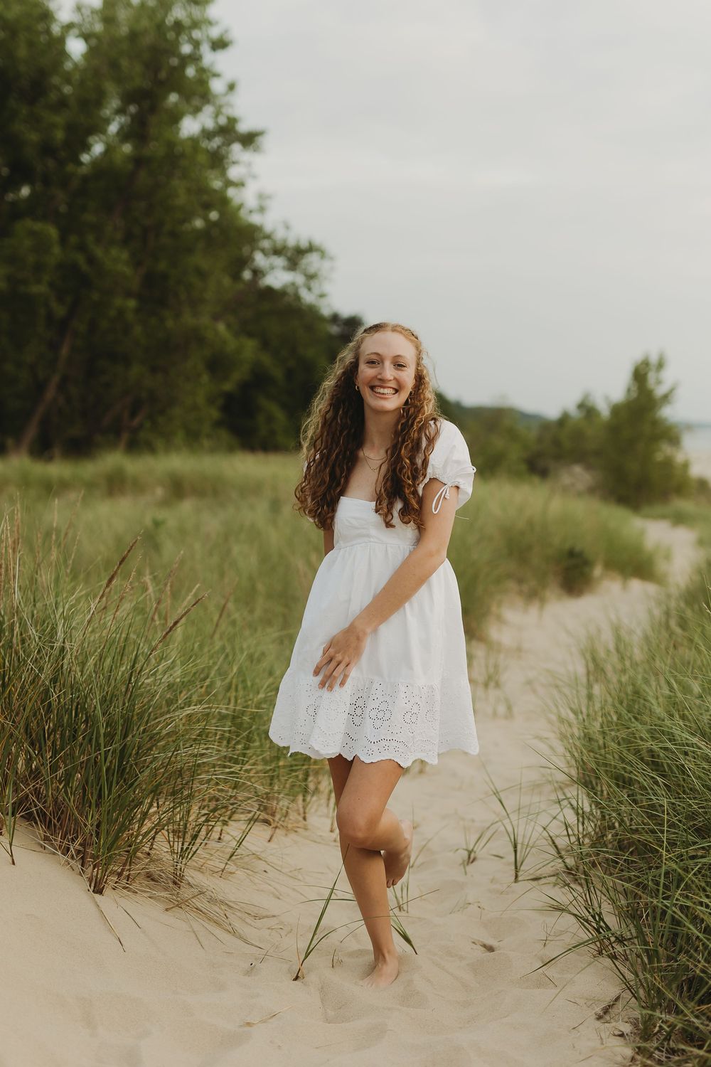 Ethereal white dress sways in the breeze as a person twirls joyfully among sand dunes and beach grass at sunset.