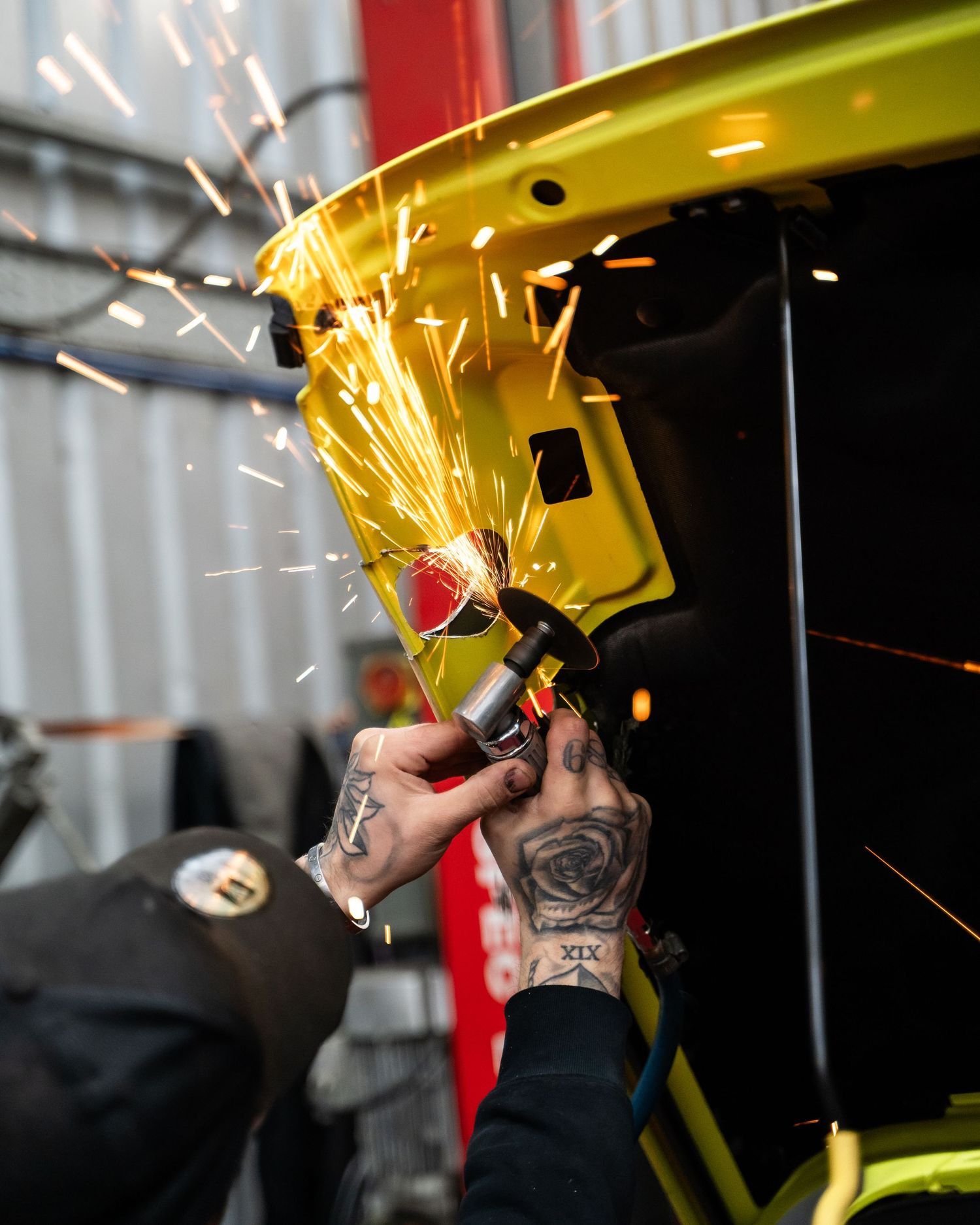 Metal grinding creates bright sparks while working on yellow automotive panel.