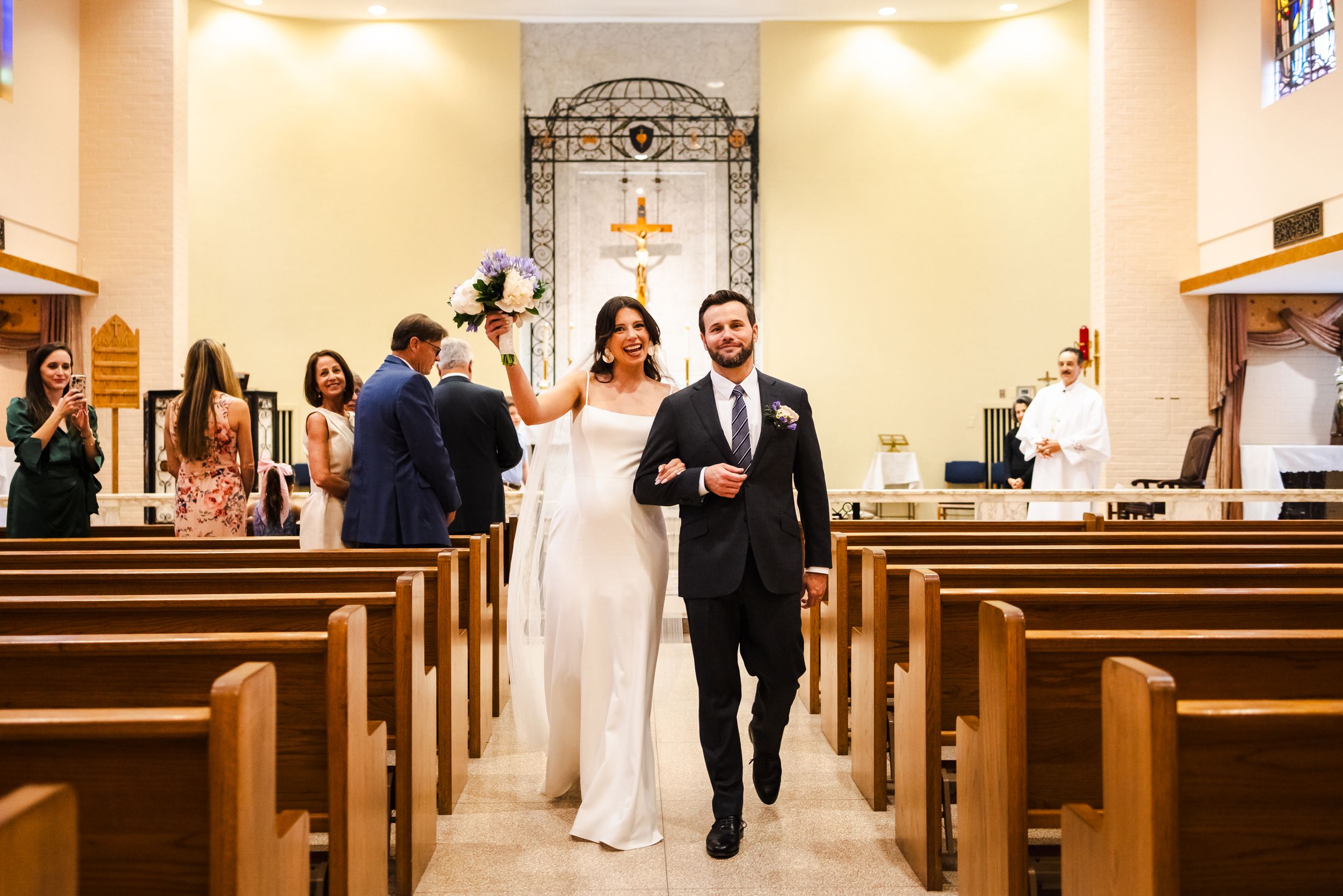 A wedding ceremony in a church with wooden pews and decorative iron archway.