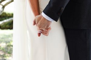 Close-up of newlyweds holding hands showing wedding rings and formal attire.
