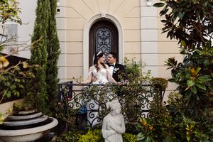 Elegant wedding photography session in front of Mediterranean-style building with cypress trees.