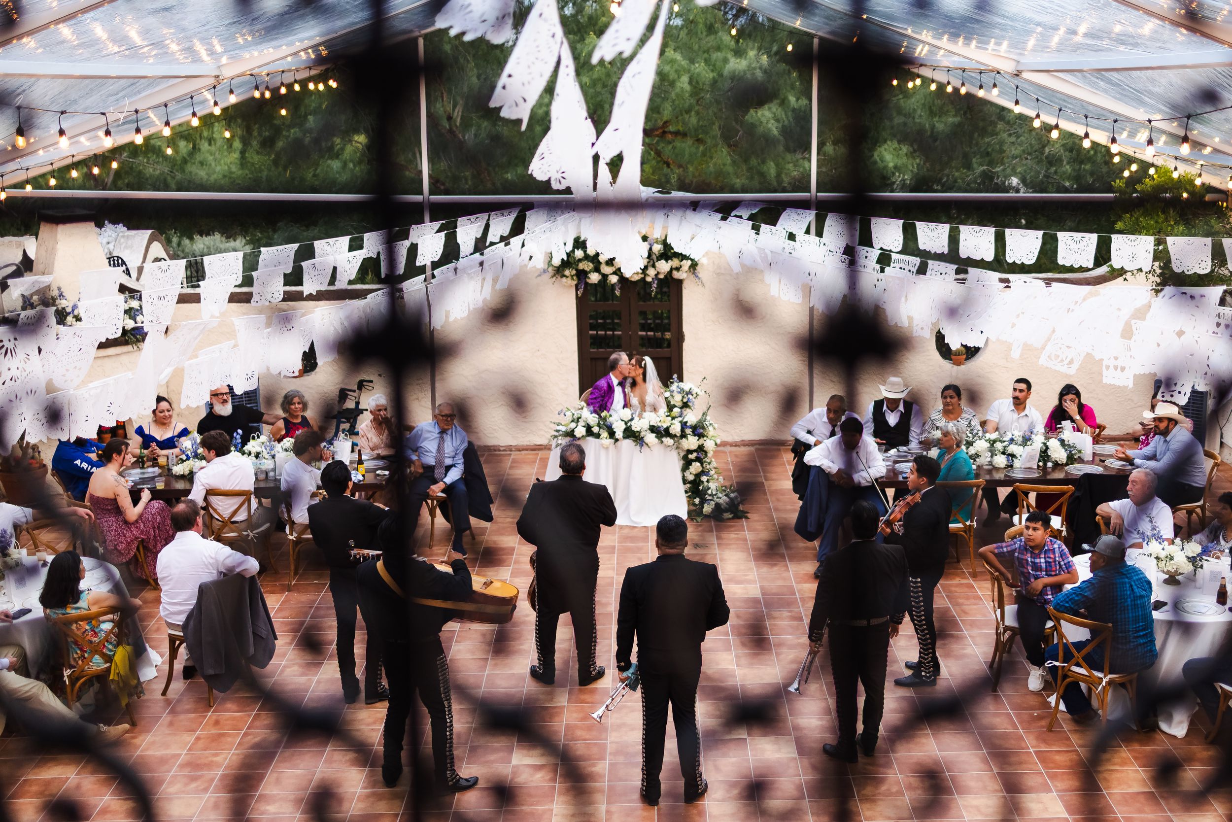 An outdoor wedding reception under a tent with string lights and guests mingling.