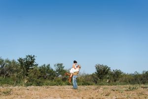 A playful engagement photo against a bright blue sky in an open field.