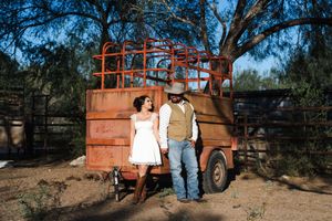 Couple poses together against rustic orange truck and desert landscape during sunset photoshoot.