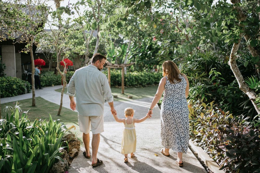 A family holding hands while walking along a sunlit garden pathway.