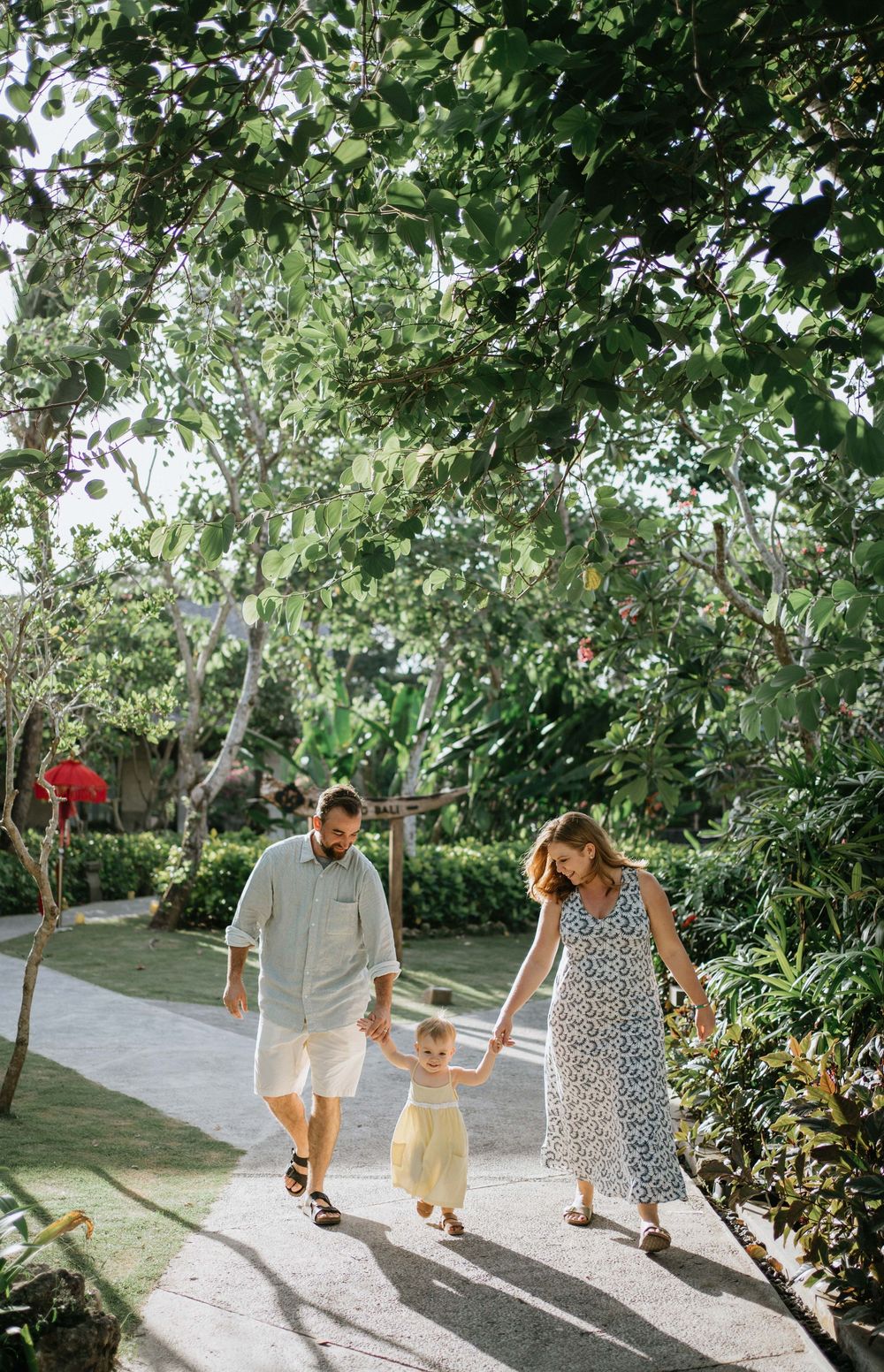 Family members walking together on a sunlit garden path surrounded by lush greenery.